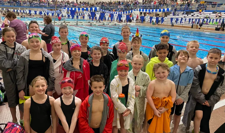 A group of swim team kids pose on the pool deck at the state meet