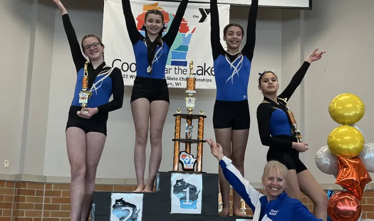 Four young gymnasts and a coach pose on a podium