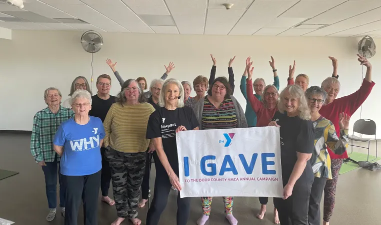 A group of YMCA members celebrates with outstretched arms as a banner is held up with the text "I Gave"
